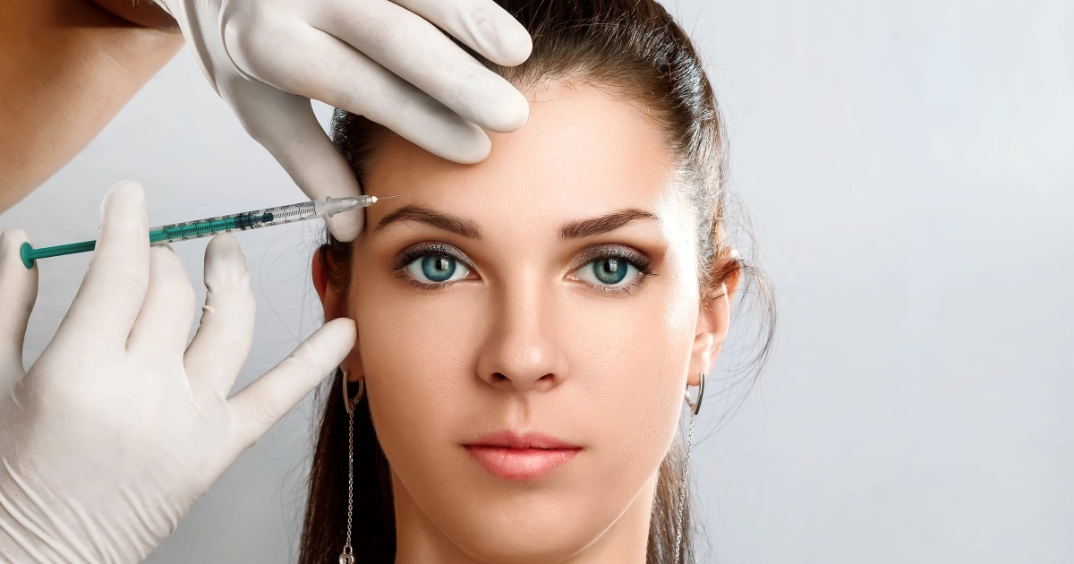 A woman receiving a Botox injection in Houston, TX, near her forehead, possibly a cosmetic filler or neuromodulator.